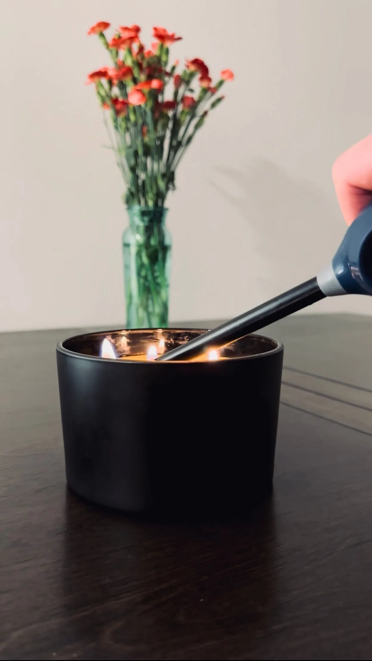 A candle being carefully tended in a matte black jar
