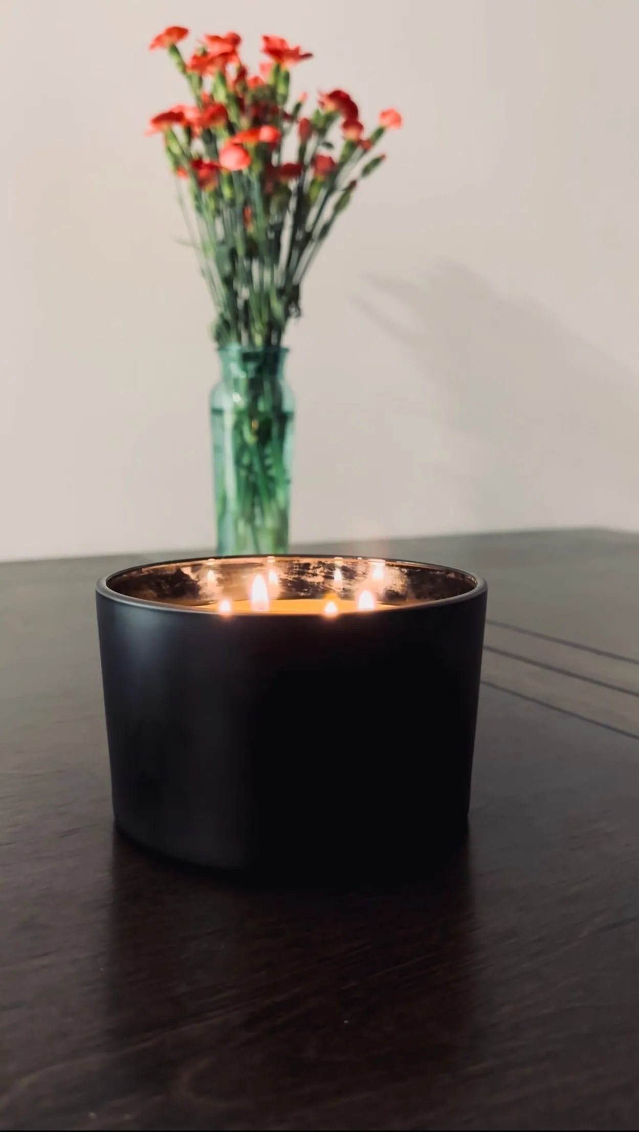 A matte black beeswax candle glowing on a table beside fresh flowers